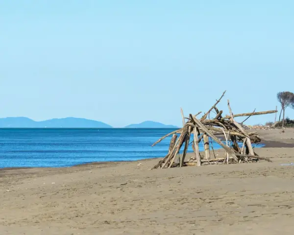 Spiaggia selvaggia nel Parco Regionale della Maremma con un rifugio di legni sulla sabbia e il mare blu all'orizzonte.