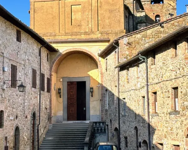 Chianni cosa vedere: un vicolo con case in pietra, una chiesa con un grande portale in legno e una scalinata.