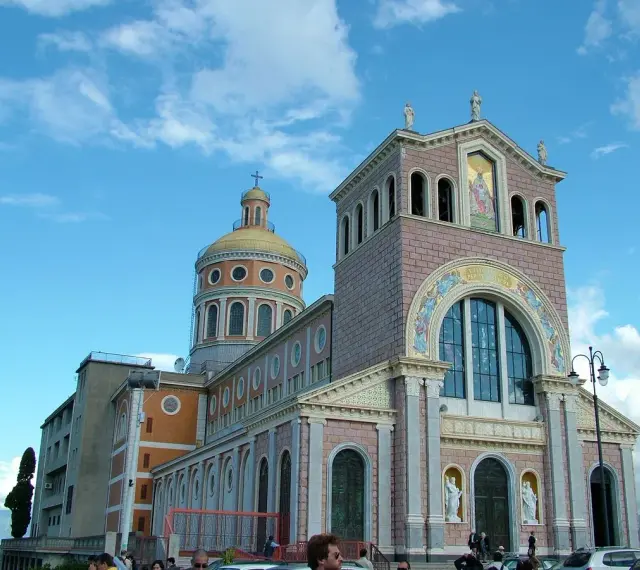 Imponente Santuario di Tindari con cupola dorata e facciata decorata, sotto un cielo azzurro con nuvole bianche.