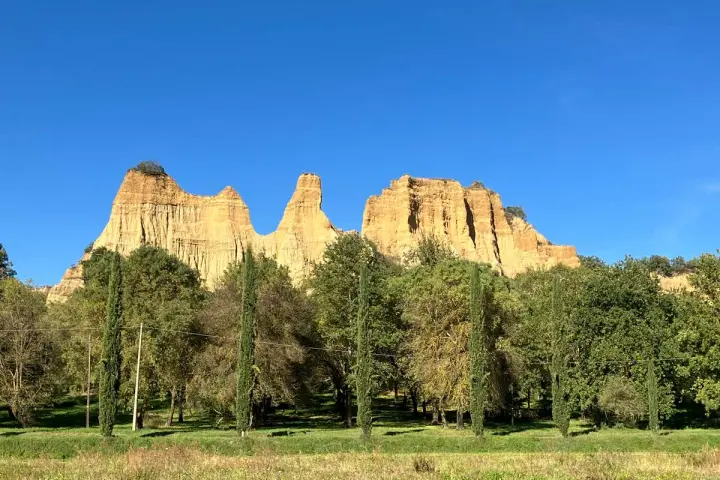 Le maestose balze del Valdarno si ergono sotto un cielo azzurro, circondate da una rigogliosa vegetazione e cipressi slanciati.