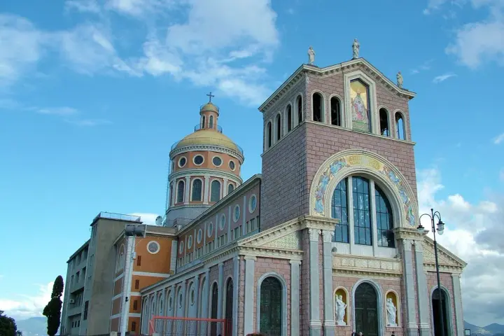 Imponente Santuario di Tindari con cupola dorata e facciata decorata, sotto un cielo azzurro con nuvole bianche.