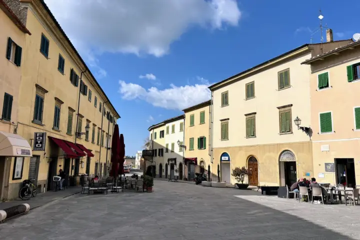 Piazza tranquilla a Pomarance, cosa vedere: edifici storici con persiane verdi, tavolini all'aperto di un bar.