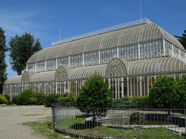 Serra in vetro con archi decorati, parte del giardino orticoltura firenze, circondata da alberi e vegetazione.