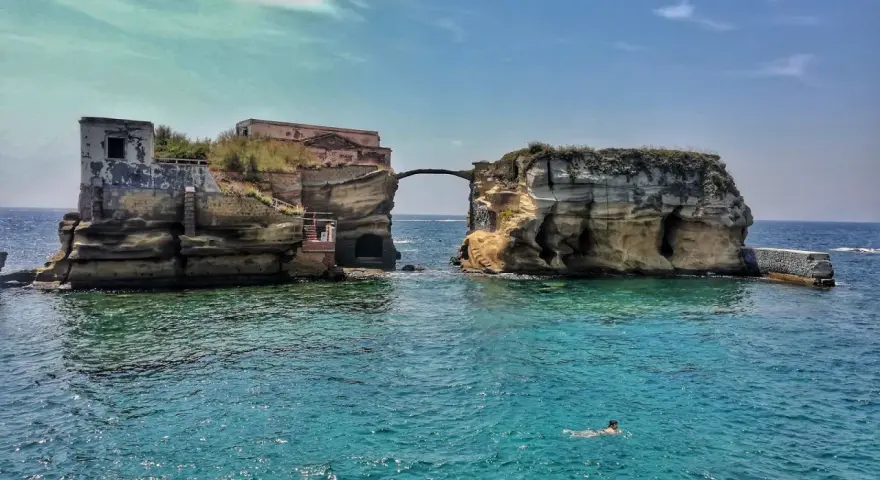 L'isola di Gaiola, con le sue rovine suggestive e il mare cristallino, accoglie bagnanti e nuotatori in una giornata di sole.