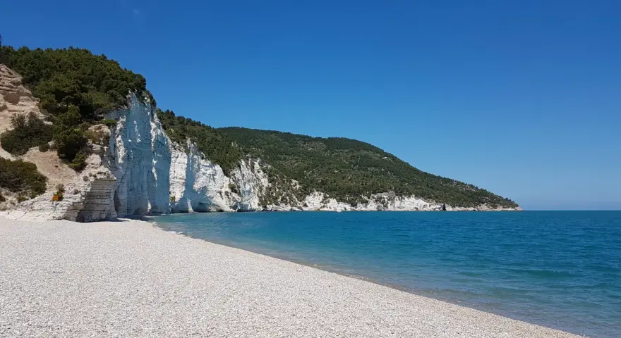 Scogliera bianca a picco sul mare turchese, con una spiaggia di ciottoli bianchi. Un angolo di paradiso, la spiaggia bianca Puglia.