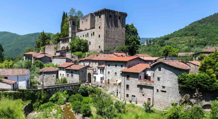 Fivizzano cosa vedere: un borgo medievale con castello, case in pietra e un ponte ad arco su un ruscello.