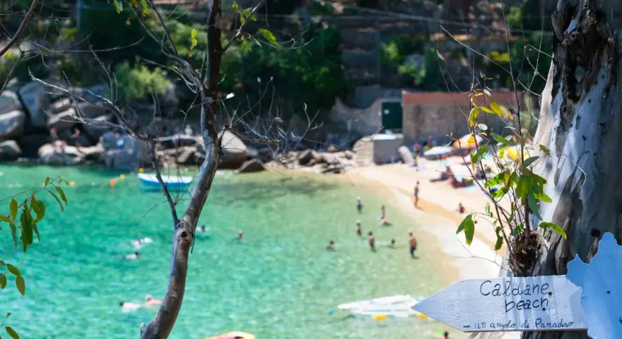 Segnale per le spiagge di Caldane, Isola del Giglio, indica un angolo di paradiso con gente che nuota nell'acqua cristallina.