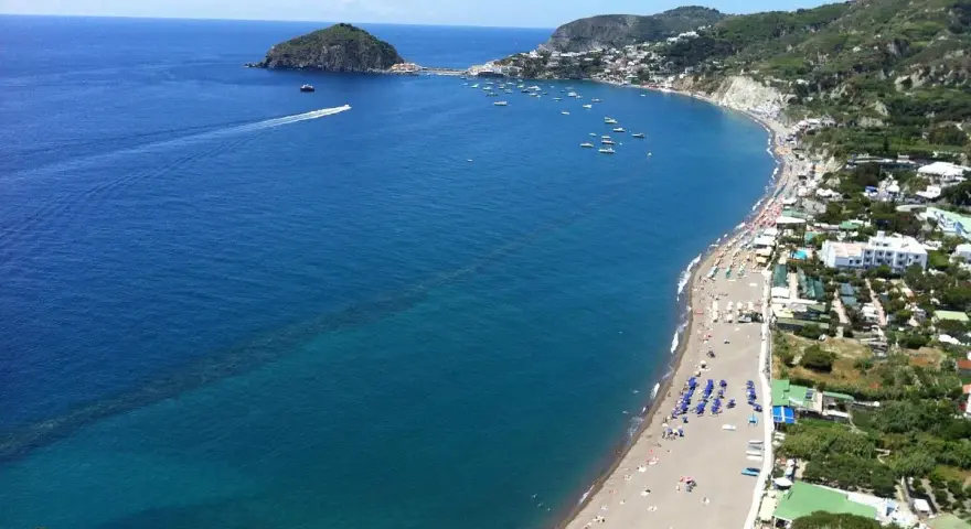 Vista panoramica della spiaggia dei Maronti, con il mare blu intenso, tante barche e la costa verdeggiante.