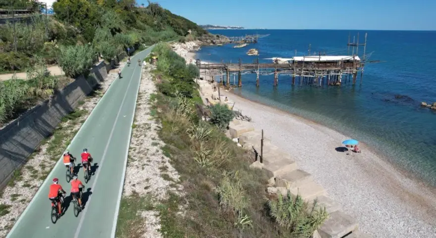 Ciclisti sulla pista ciclabile lungo mare, con i trabocchi che caratterizzano la costa dei Trabocchi cosa vedere. Spiaggia di ciottoli e mare azzurro.