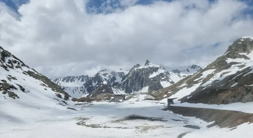 Paesaggio innevato al Gran San Bernardo con edifici storici e montagne maestose sotto un cielo nuvoloso.