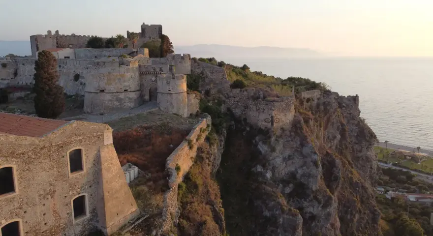 Il complesso monumentale del castello di Milazzo si erge su una scogliera a picco sul mare, con torri e mura antiche che dominano il paesaggio.