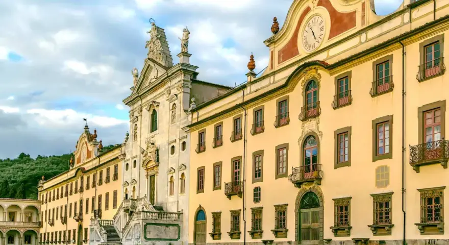 La maestosa Certosa di Calci, con la sua facciata imponente e il prato verde antistante, incanta sotto un cielo nuvoloso.