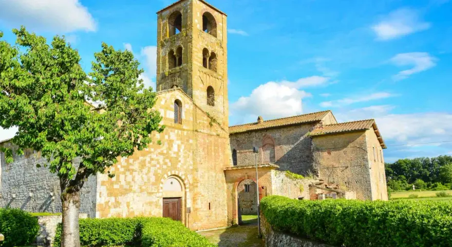 Antico campanile romanico e edifici in pietra nel **Sovicille centro storico**, con un albero verdeggiante e cielo azzurro.
