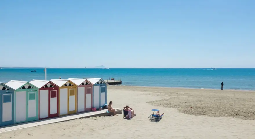 Colorate cabine sulla spiaggia di Ostia, mare di Roma, con persone che si rilassano al sole.