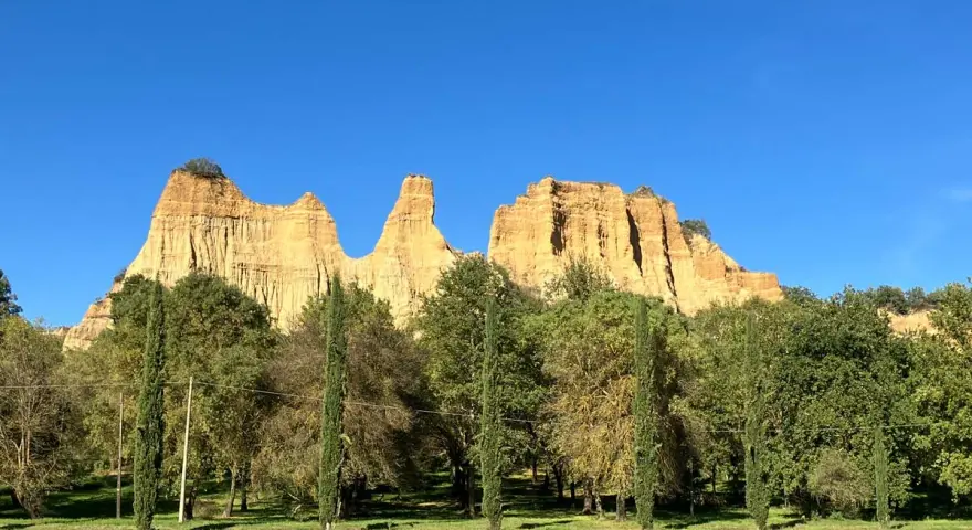 Le maestose balze del Valdarno si ergono sotto un cielo azzurro, circondate da una rigogliosa vegetazione e cipressi slanciati.