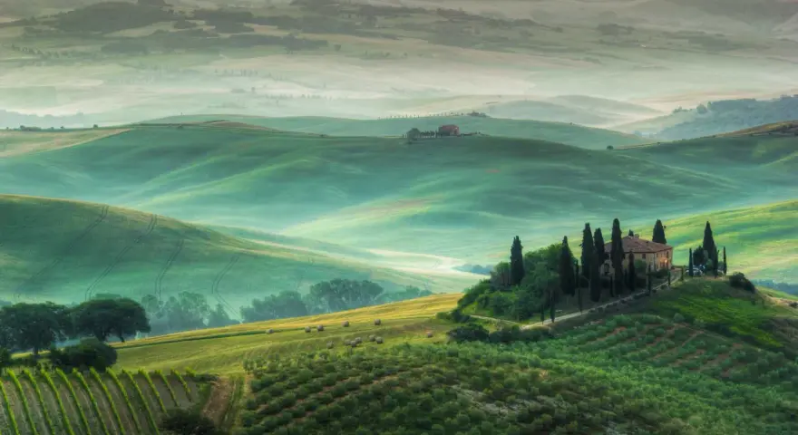 Dolci colline verdi del Val d'Orcia, con una casa colonica in cima a una collina e cipressi. Un paesaggio da cartolina, uno dei tanti punti panoramici mozzafiato.