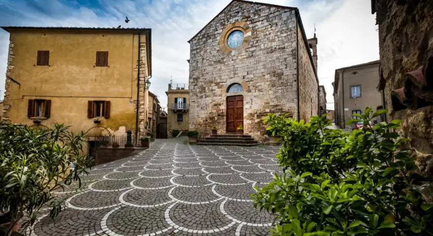 Piazza di Bibbona, cosa vedere: chiesa in pietra con rosone, case gialle e pavimentazione a ventaglio.
