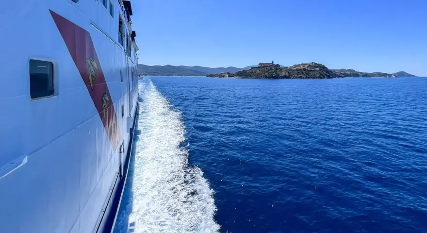 Traghetto in navigazione verso l'isola d'Elba, con la costa all'orizzonte sotto un cielo azzurro.