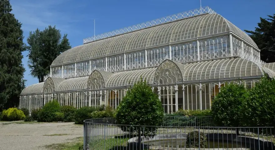 Serra in vetro con archi decorati, parte del giardino orticoltura firenze, circondata da alberi e vegetazione.
