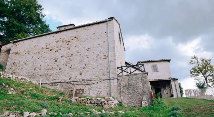 Antico eremo di Cerbaiolo, con muri in pietra grezza e vegetazione rigogliosa che sale sul pendio.