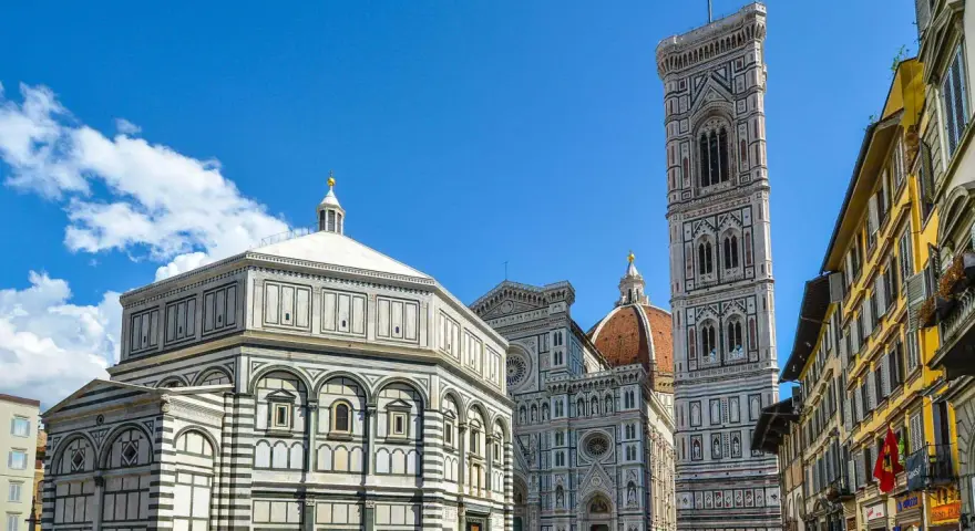 La piazza del Duomo a Firenze con il Battistero, il Campanile di Giotto e la cupola del Brunelleschi sotto un cielo azzurro.