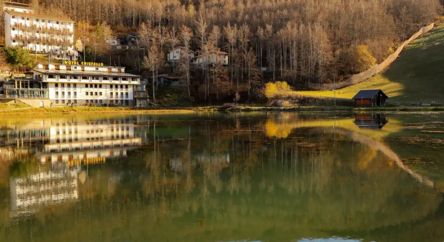 Hotel Cristallo sul Passo del Cerreto, riflesso sull'acqua calma di un lago circondato da boschi autunnali.