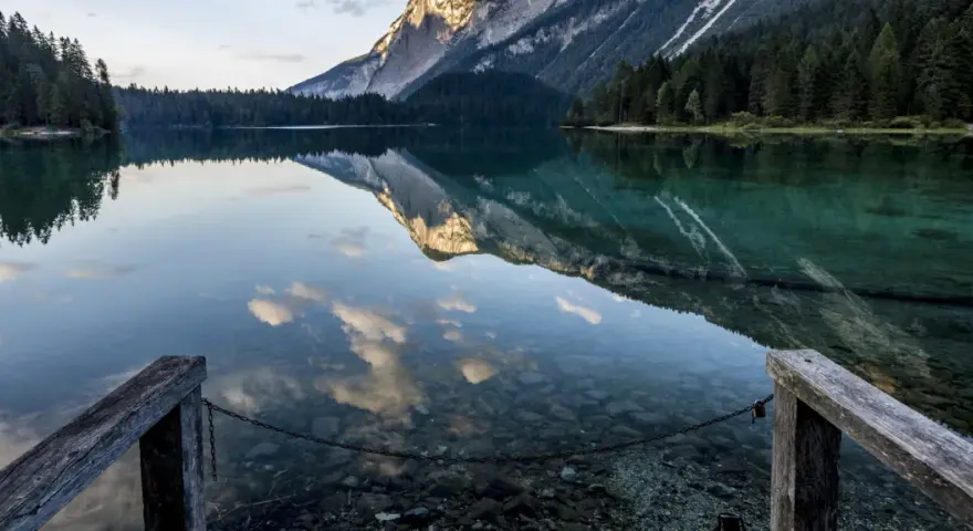 Lago alpino con riflessi di montagne e nuvole, un pontile in legno invita a contemplare la bellezza del Val di Non.