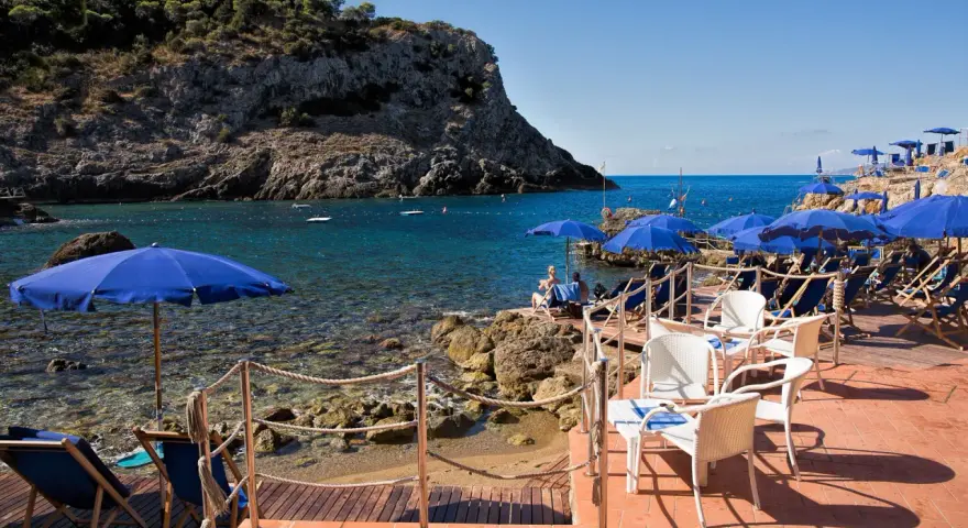 Le argentario spiagge più belle, con ombrelloni blu e lettini su una terrazza in legno, affacciate sul mare cristallino.