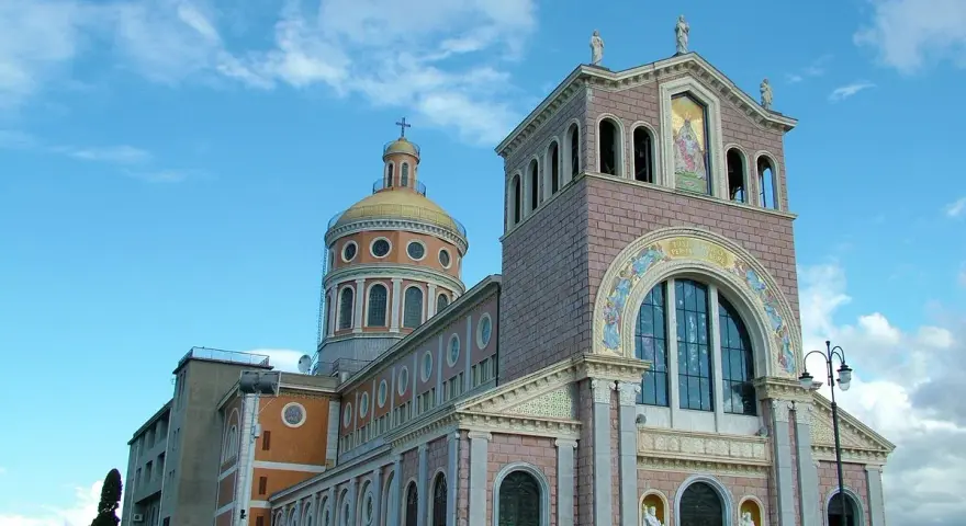 Imponente Santuario di Tindari con cupola dorata e facciata decorata, sotto un cielo azzurro con nuvole bianche.