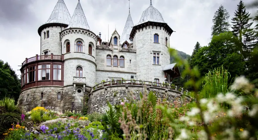 Un fiabesco castello in pietra, tra i castelli Val d'Aosta, circondato da un giardino fiorito e boschi rigogliosi.