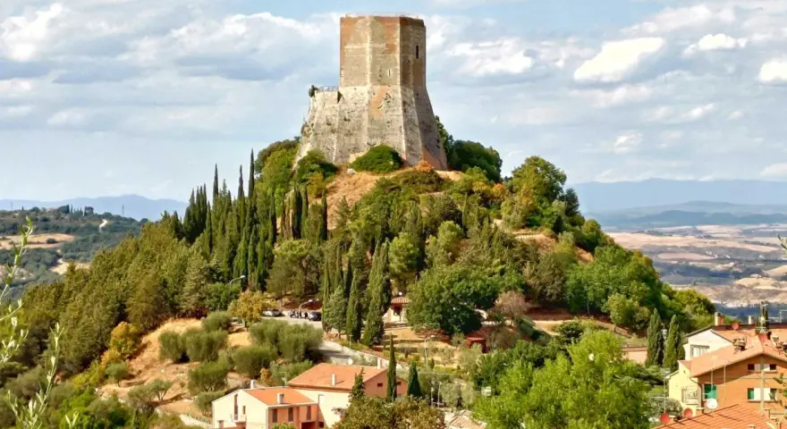 La rocca di Tentennano domina la collina, circondata da cipressi e ulivi. Sotto, un borgo con tetti rossi si adagia nel paesaggio toscano.