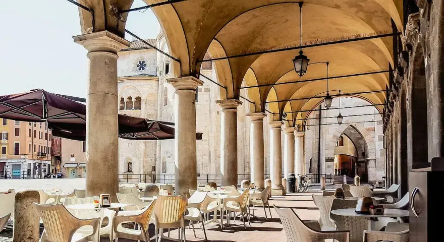 Tavolini all'aperto sotto un portico con vista sul Duomo. Un'idea su cosa fare a Modena: godersi un caffè in piazza.