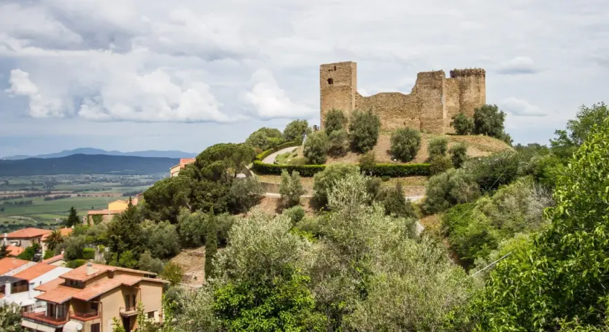 Rovine di un castello dominano il **Scarlino centro storico**, circondato da ulivi e case con tetti rossi.