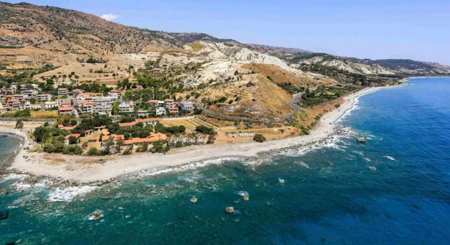 Paesaggio mozzafiato sulla costa ionica Calabria: case con tetti rossi, spiaggia rocciosa e mare blu intenso.