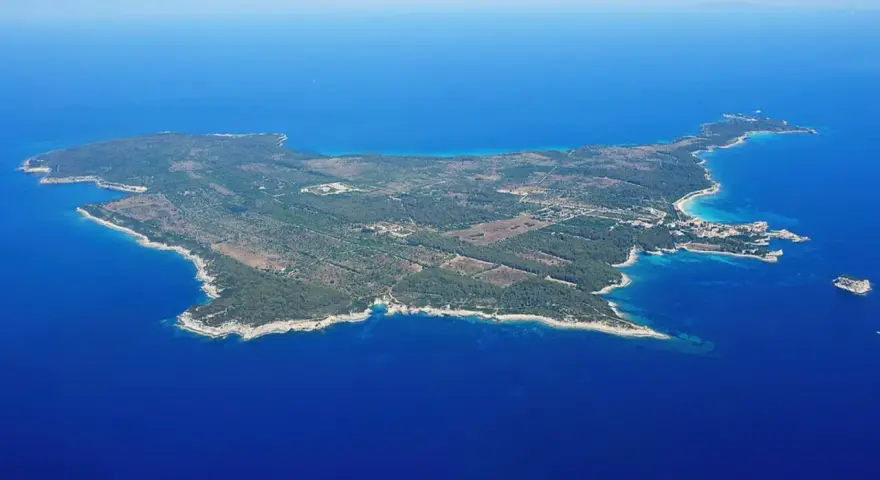 Vista aerea di un'isola verdeggiante, un'isola vicino all'Elba, con acque blu intenso e una piccola isola rocciosa in lontananza.