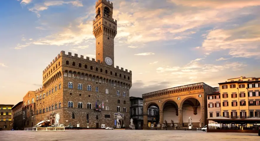 Il maestoso Palazzo Vecchio domina Piazza della Signoria, con la sua torre imponente che svetta sotto un cielo al tramonto.