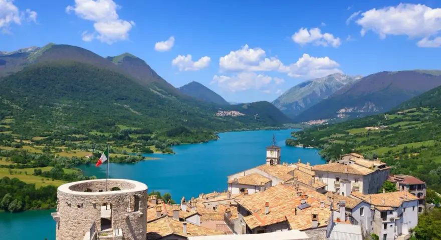 Villetta Barrea: cosa vedere? Un borgo con torre medievale, tetti rossi e un lago azzurro circondato da montagne verdi.