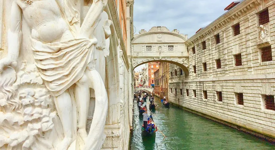 Gondole scivolano sul canale sotto il Ponte dei Sospiri, con un'imponente statua in primo piano.