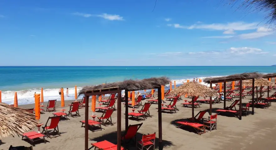 Spiaggia attrezzata a Marina di Bibbona, con lettini rossi, ombrelloni di paglia e il mare azzurro all'orizzonte.