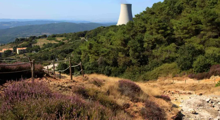Sentiero nel parco delle Biancane con torretta di raffreddamento in lontananza, circondato da vegetazione e colline.