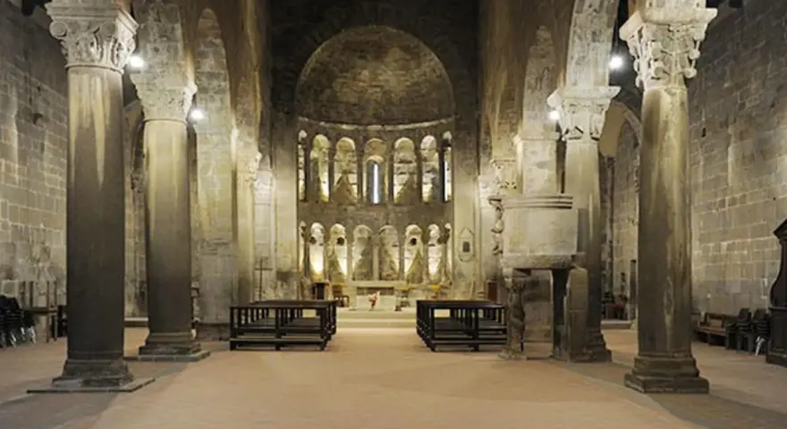 Interno della pieve di Gropina, con imponenti colonne, archi e un'abside decorata.