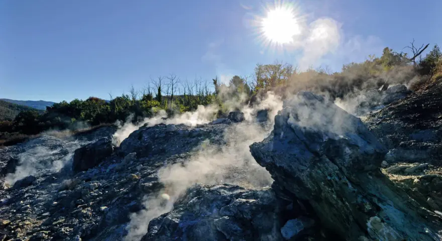 Fumarole attive nel **Val di Cecina**, con vapore che sale tra le rocce sotto un sole splendente.