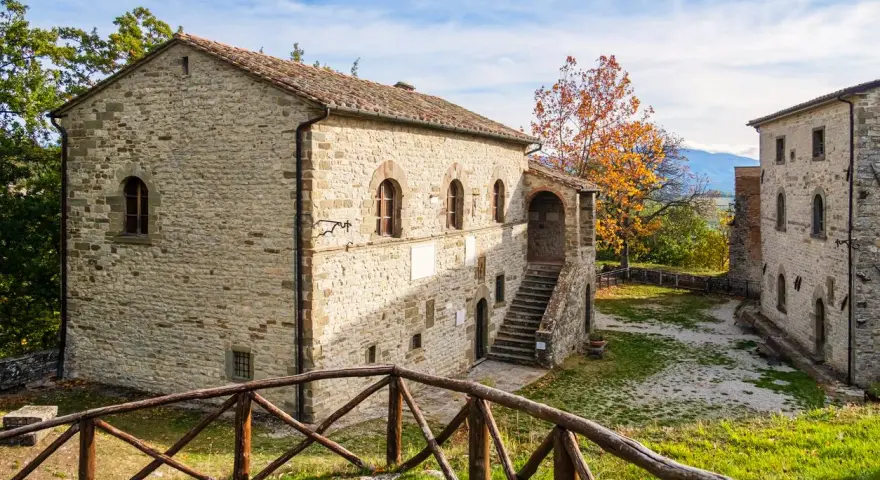 Antica strada in Casentino conduce a un borgo in pietra con un cortile interno e un albero dalle foglie arancioni.