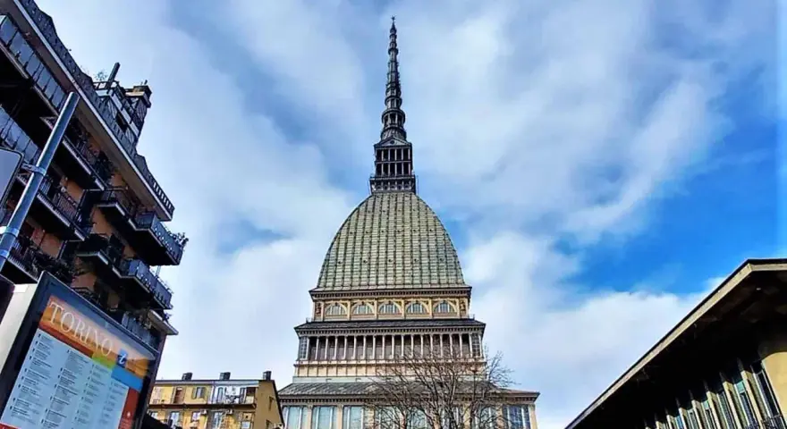 La Mole Antonelliana svetta maestosa nel cielo azzurro di Torino, circondata da edifici moderni e storici.