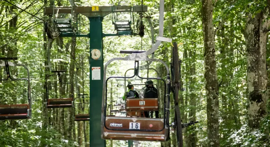 La funivia Monte Amiata trasporta due persone e una mountain bike tra gli alberi rigogliosi.