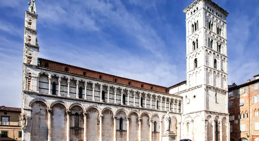 La piazza San Michele a Lucca, con la sua chiesa romanica e la torre campanaria imponente, sotto un cielo azzurro.