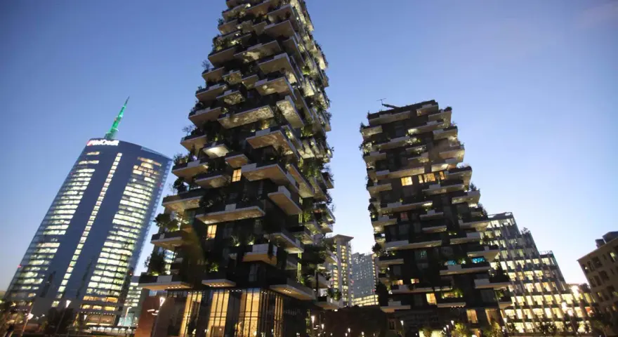 Il Bosco Verticale di Milano, con i suoi grattacieli ricoperti di alberi e piante, si staglia contro il cielo serale.
