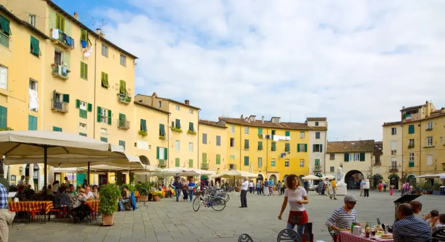 Passeggiata nella storica piazza anfiteatro di Lucca, con i suoi palazzi gialli e i tavolini all'aperto.