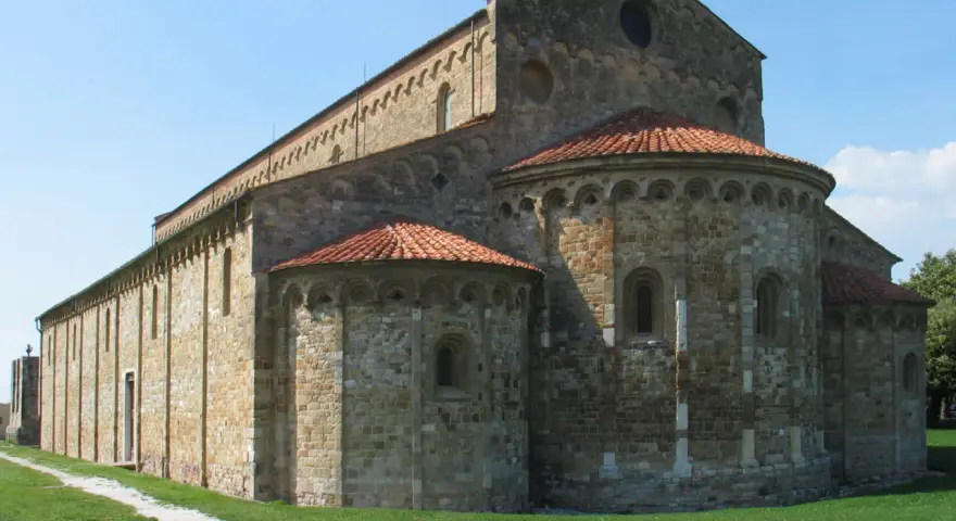Antica basilica romanica di San Piero a Grado, con absidi semicircolari e tetto in cotto, immersa nel verde.