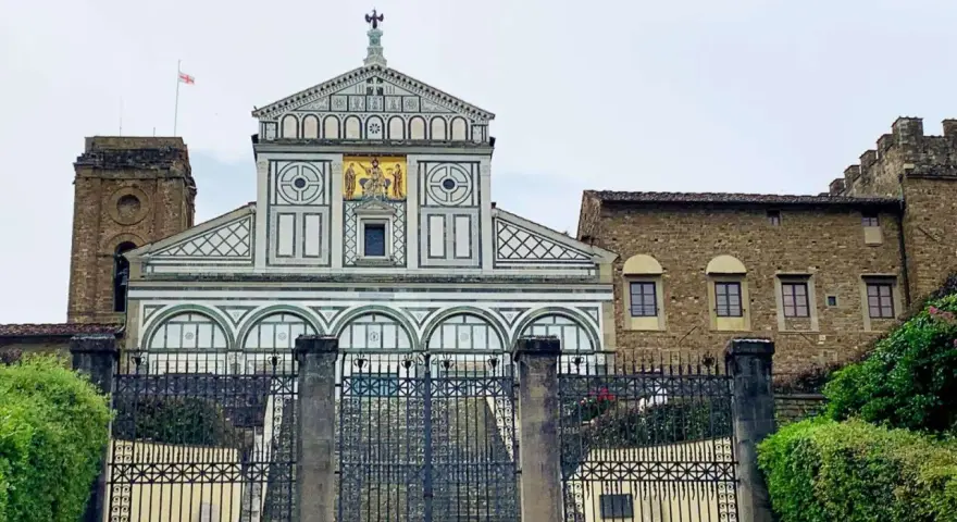 La facciata marmorea di San Miniato al Monte domina la vista, con un cancello in ferro battuto che precede la scalinata.